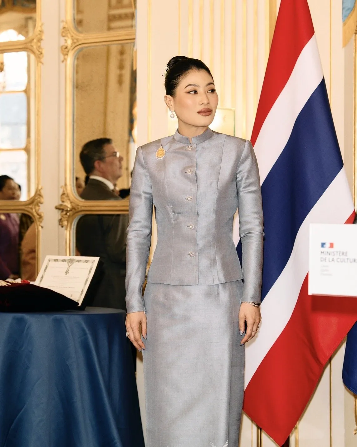 A medium portrait of the Thai princess looking off-camera. She wears a traditional grey silk dress with delicate floral embroidery at the hem.