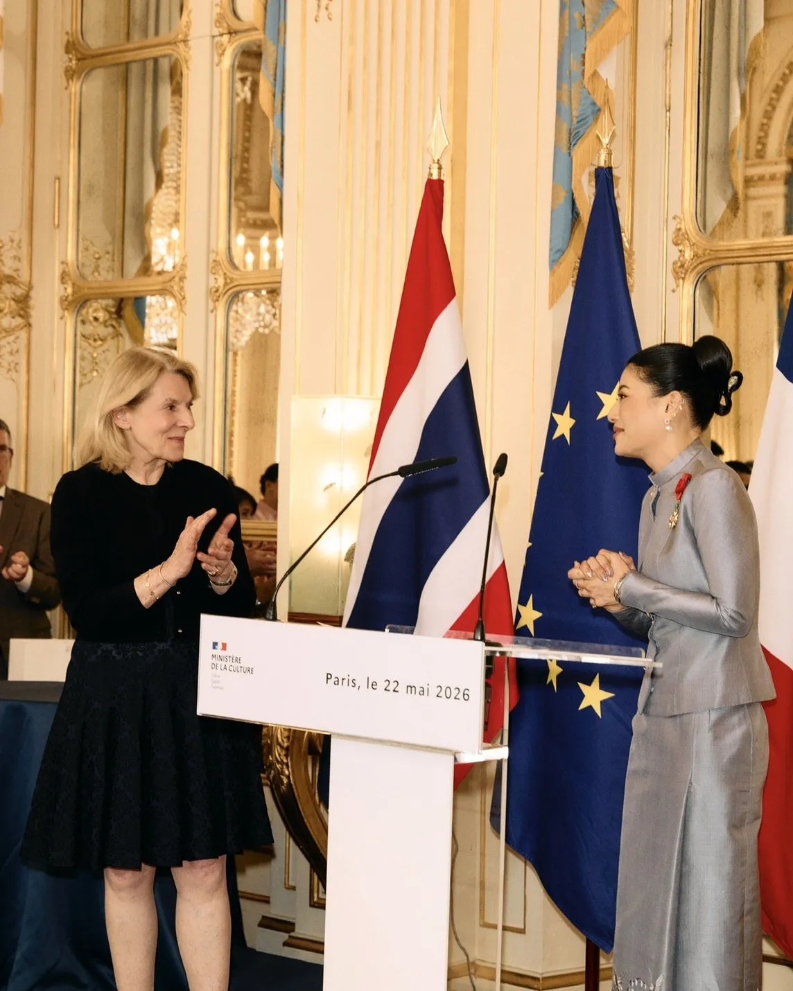 The French official claps as the princess smiles and gestures with her hands in gratitude during the official ceremony.