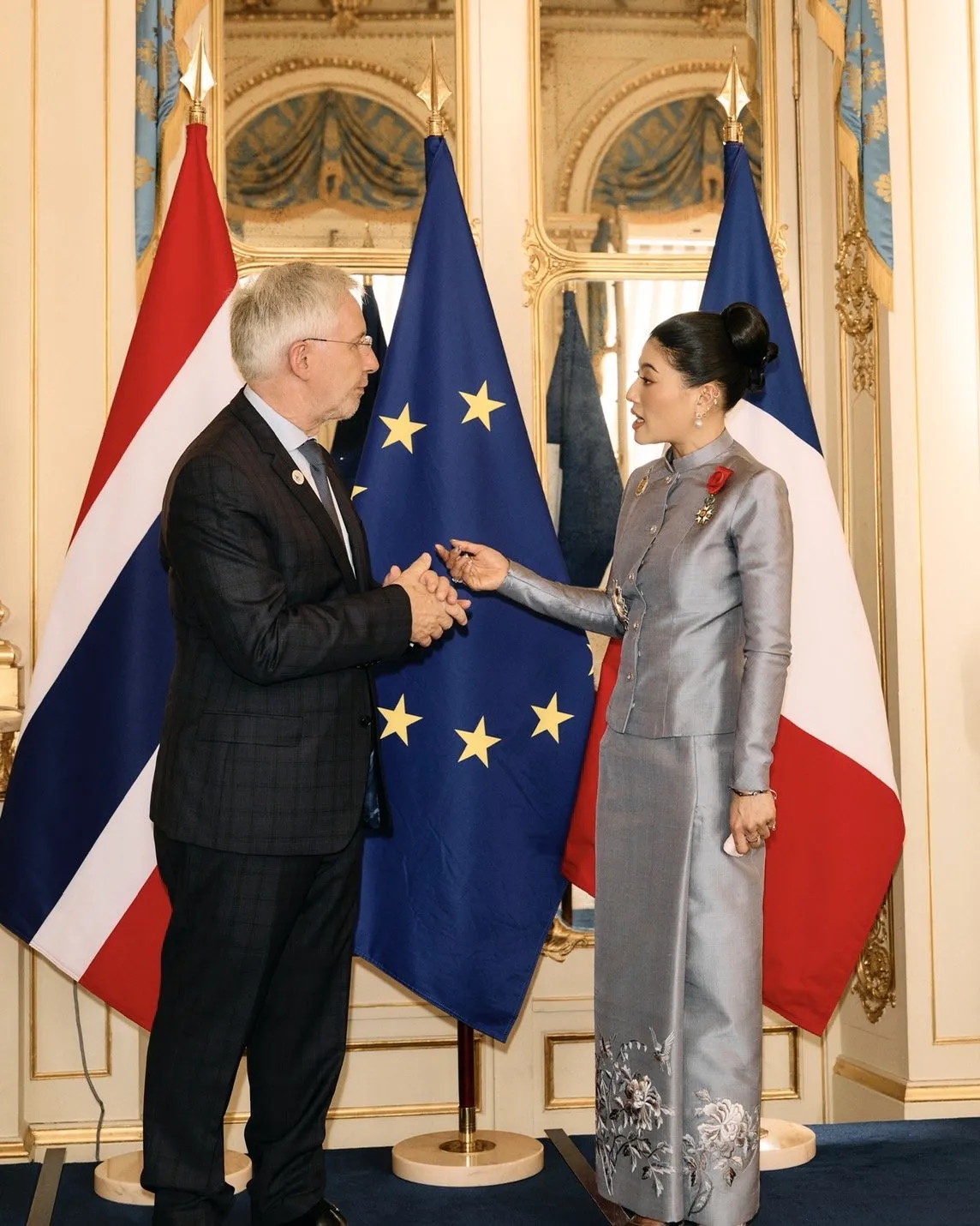 A wide group photo of the princess, French official, and Thai delegation standing before the French, EU, and Thai national flags.