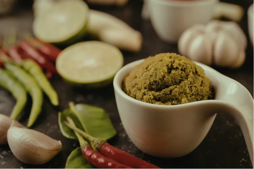 green curry paste in a ramiken next to a clove of garlic and red and green chili peppers