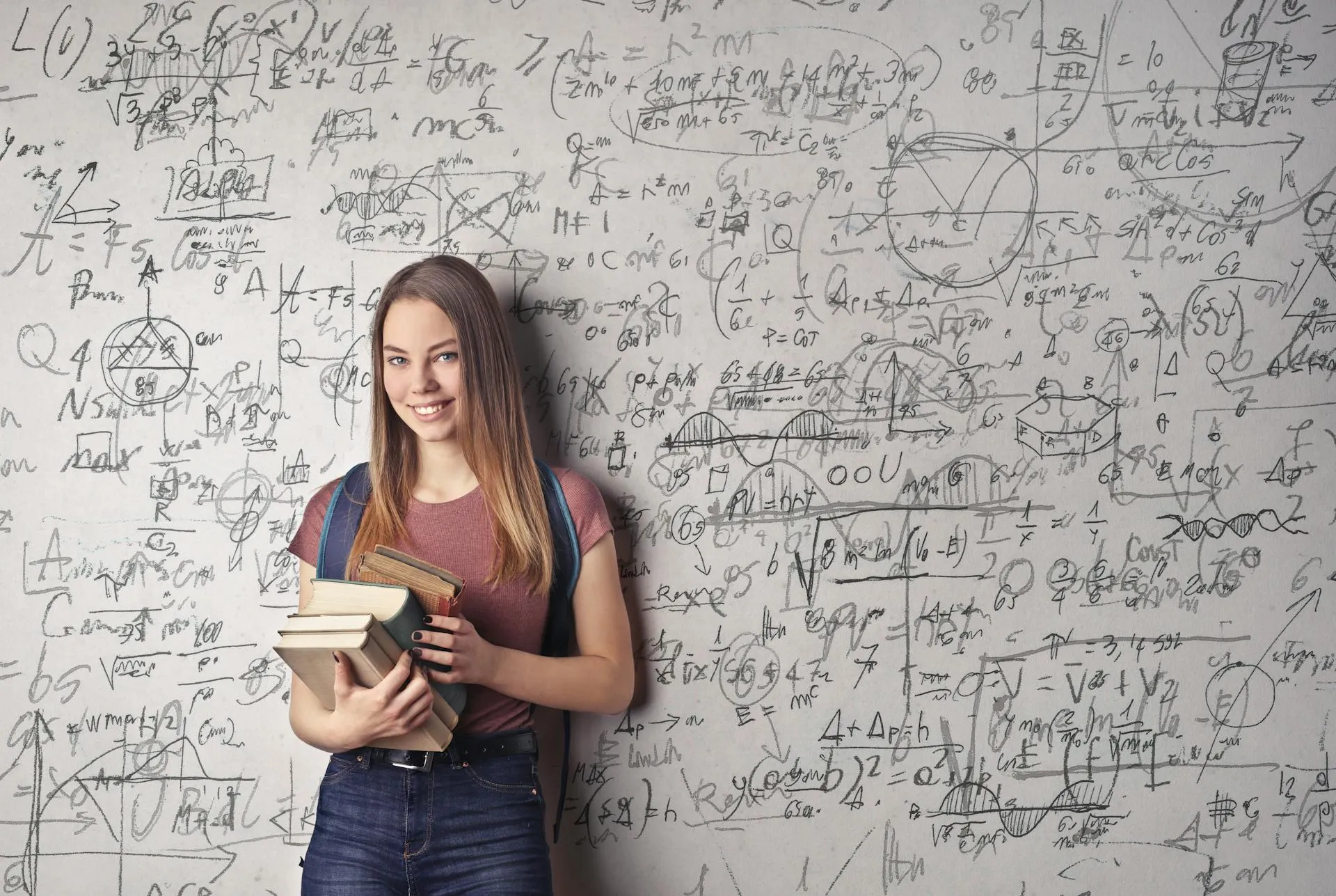 a young lady holding books in her right arm leaning her back against a white board filled with mathematics fomulars