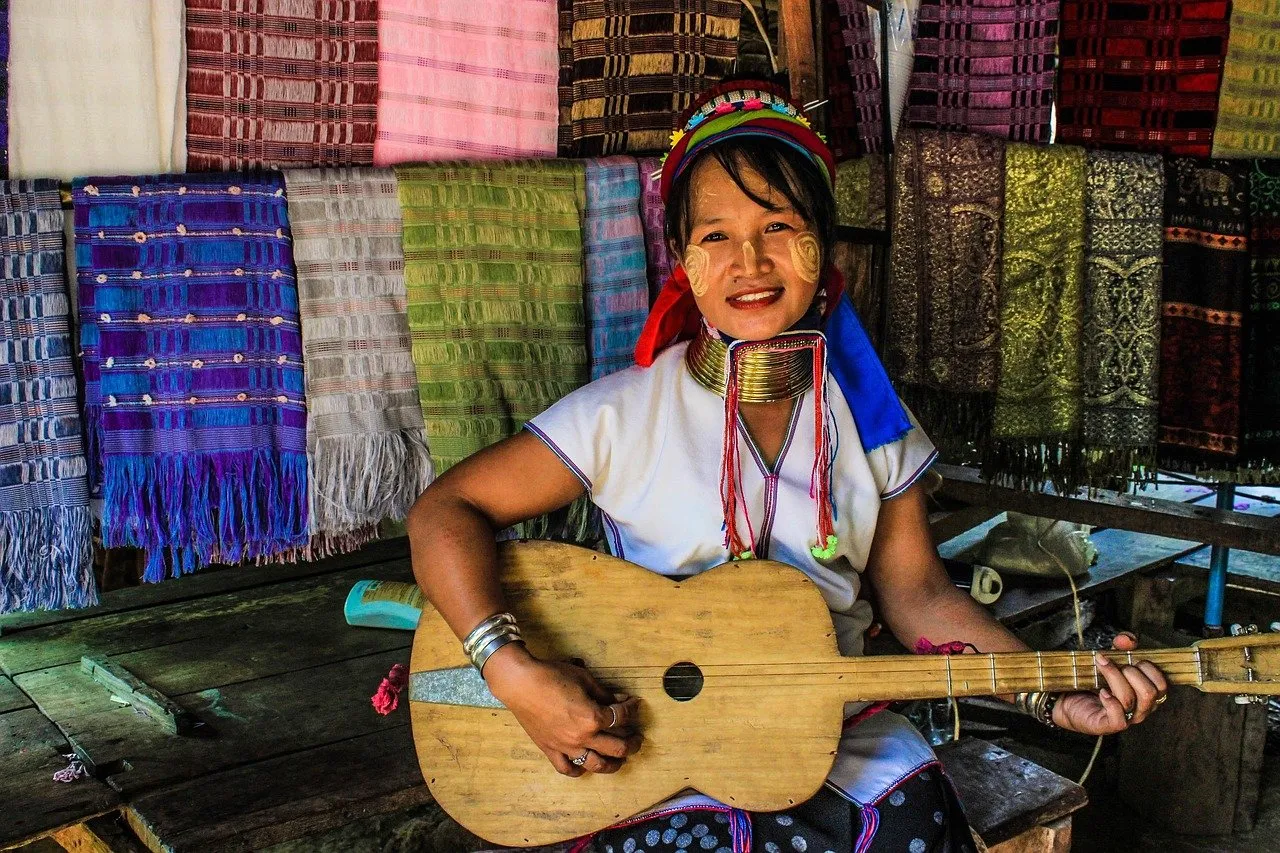 an ethnic lady wearing knit hat holding a guitar sitting in front of woven fabric.