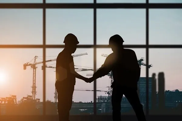 A shadow of two construction workers holding hand against the landscape of construction buildings. 