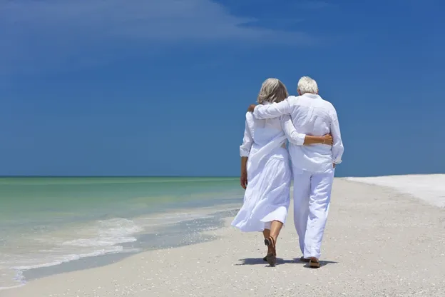 An elderly couple arm in arm walking down the beach in Thailand.