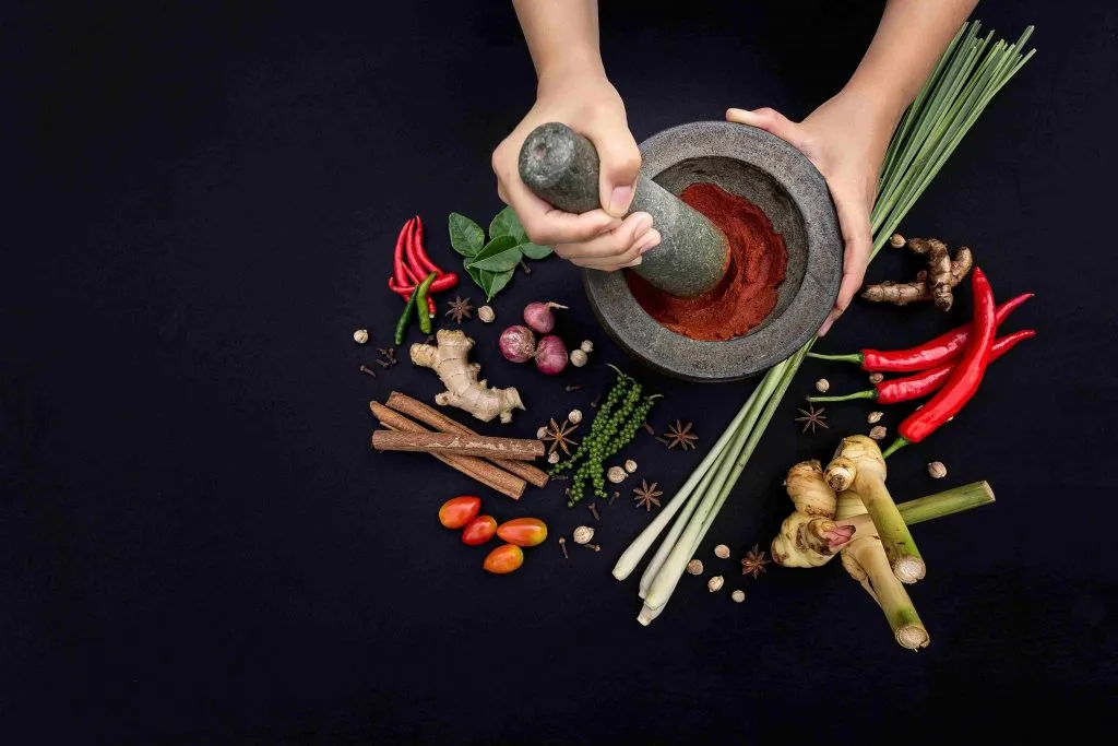 Traditional Thai granite mortar and pestle surrounded by organic Thai herbs and plants.