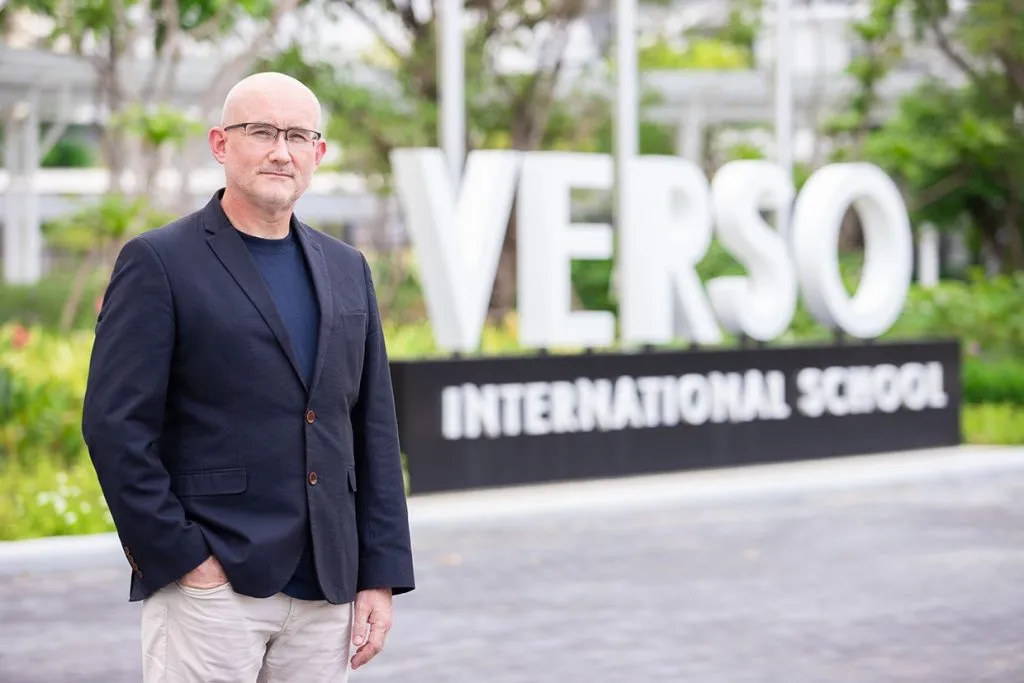 Mr. Cameron Fox, Head of VERSO International School, standing next to a sign of the school.