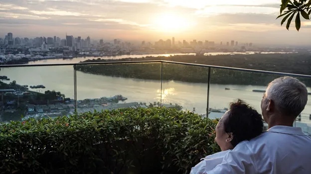 An elderly couple hugging and looking out on the Bangkok landscape.