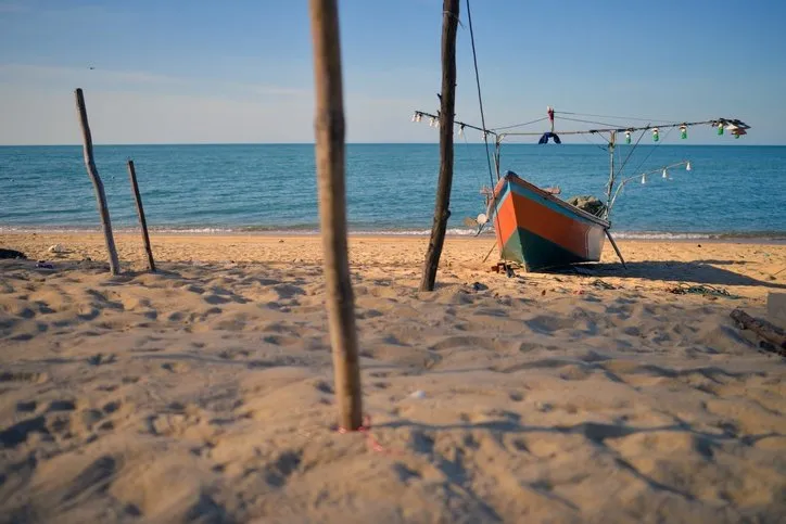 A fishing boat left on a sandy beach with wooden stakes.