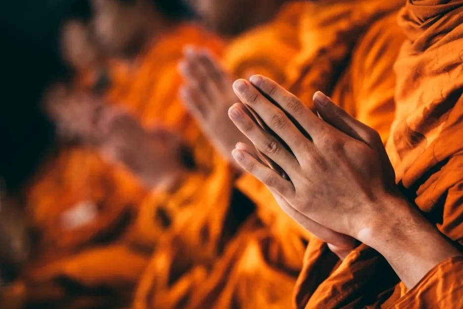 A row of seated Thai monks in praying gesture.