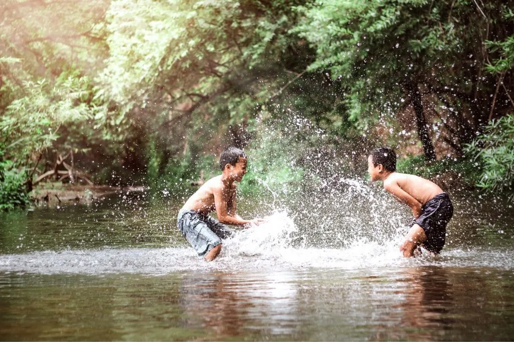 Two Thai kids splashing water in a river.