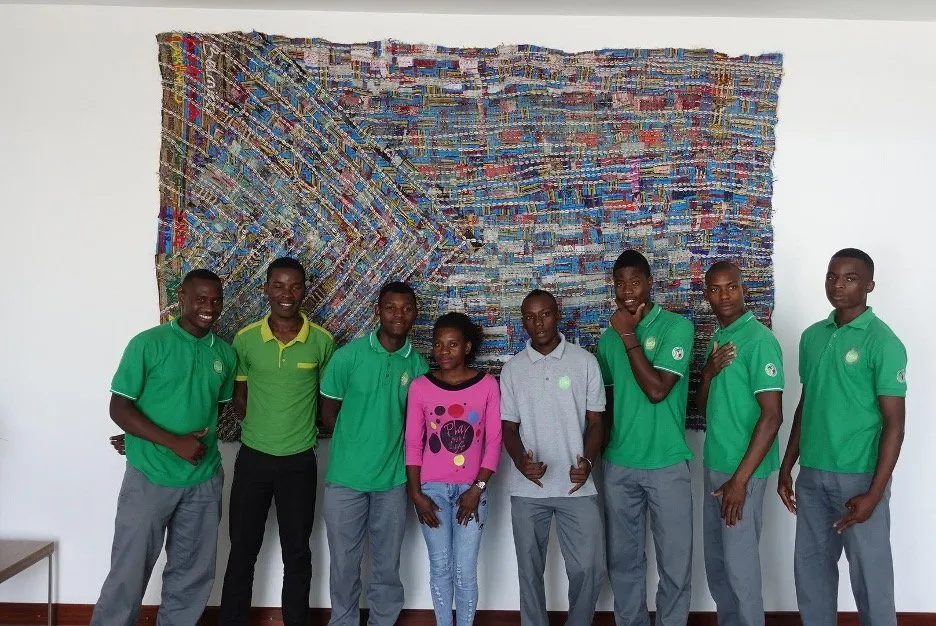 A group of people standing in front of an artwork made from discarded fabric, beach detritus, beads and sewing.