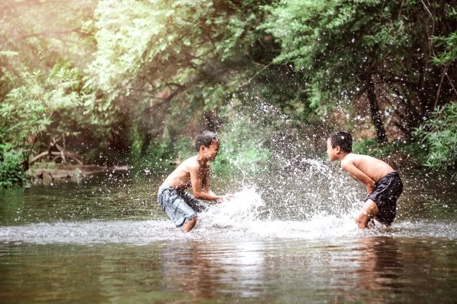 Two children playing and shaplising water in the river to combat summer heat.