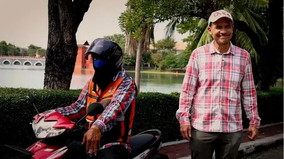 Chris standing next to a motorcycle taxi driver and explaining the finer points of getting a motorcycle taxi in Bangkok.