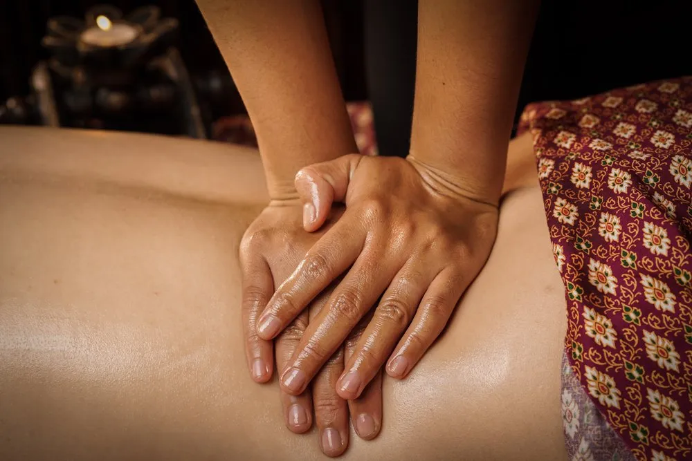 Thai massage therapist kneading a patient's lower back.