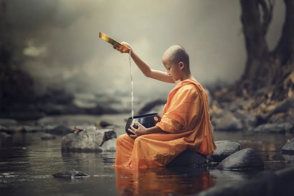 Young Buddhist monk pouring water into alms bowl.