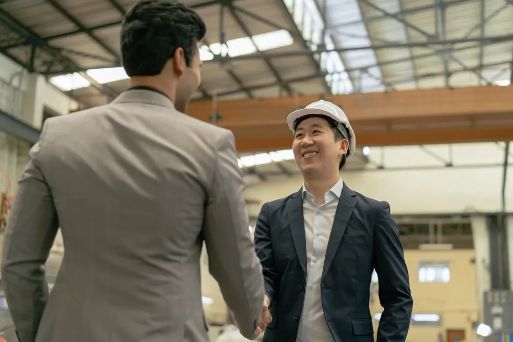 A businessman shaking hands with his employee in a factory setting
