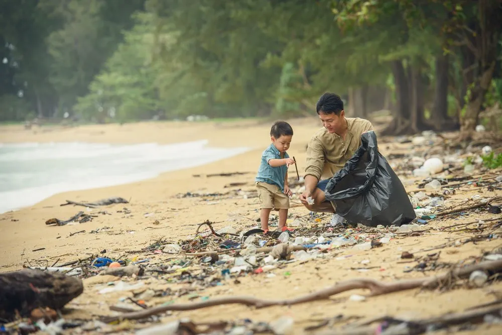 A dad and son collecting plastic bottles and trash that were left on the beach