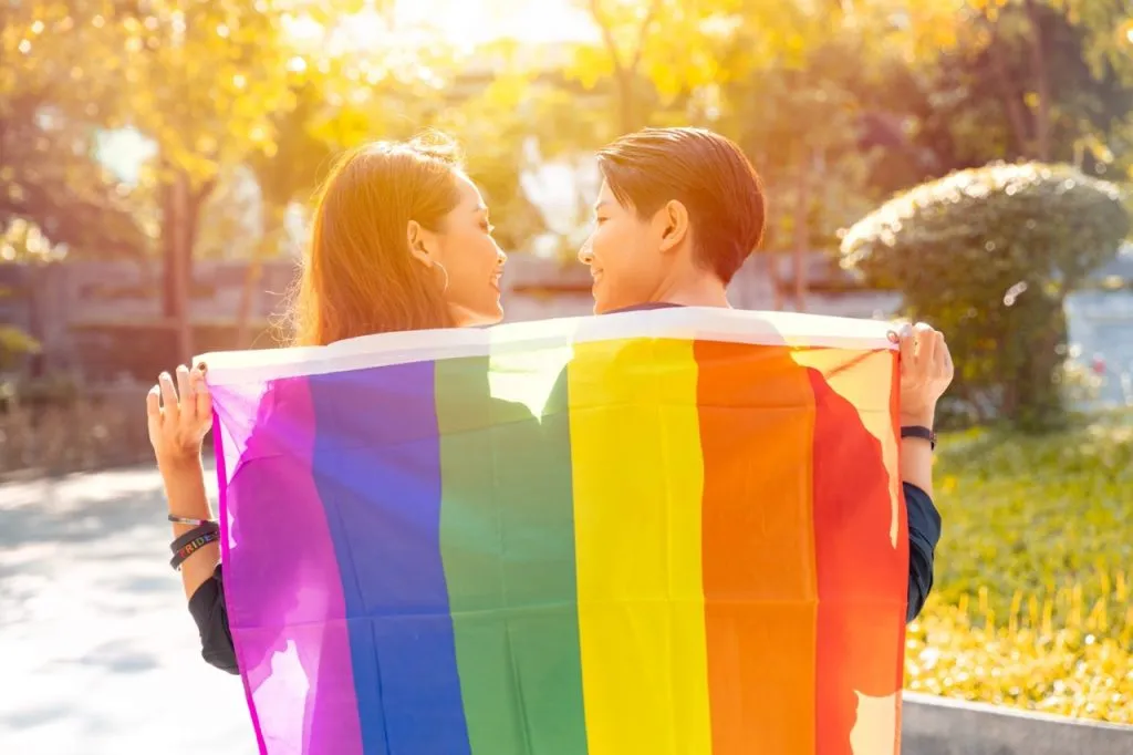 A couple looking at each other and holding a rainbow flag.