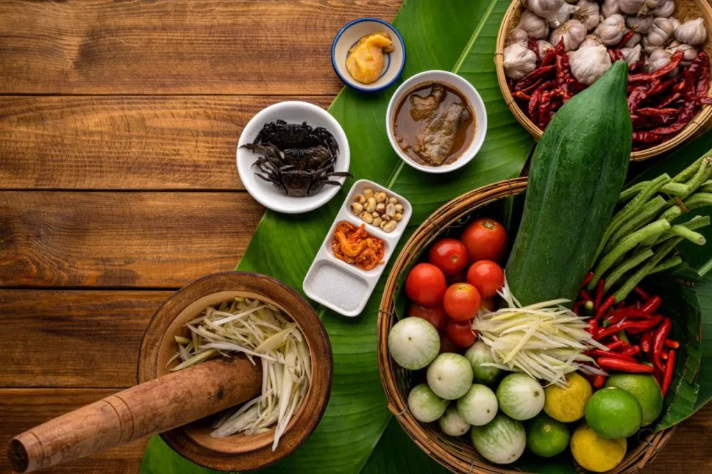 Thai papaya salad being prepared on a kitchen table with all ingredients