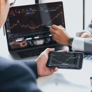 Two businessmen checking the stock market and graph on a laptop and mobile phone
