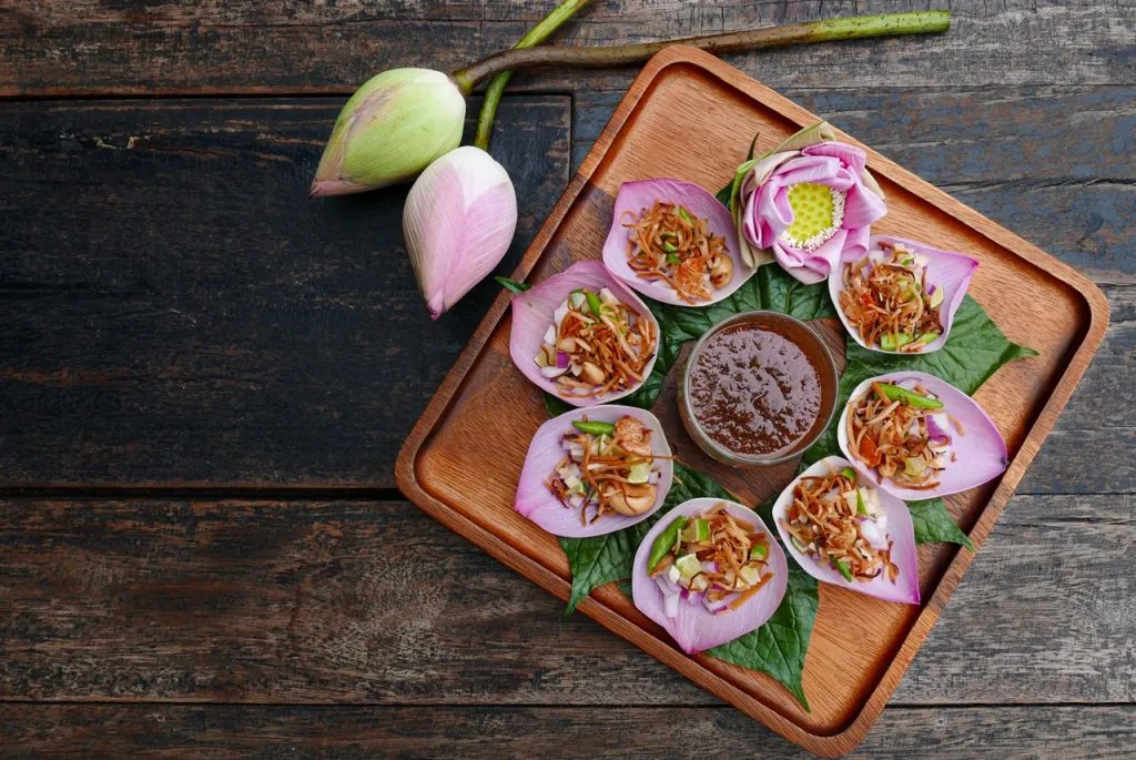 Lotus Petal Miang Kham or Miang Kham Bua Luang filled with roasted coconut shavings, shallots, chili peppers, ginger, garlic, and lime slices