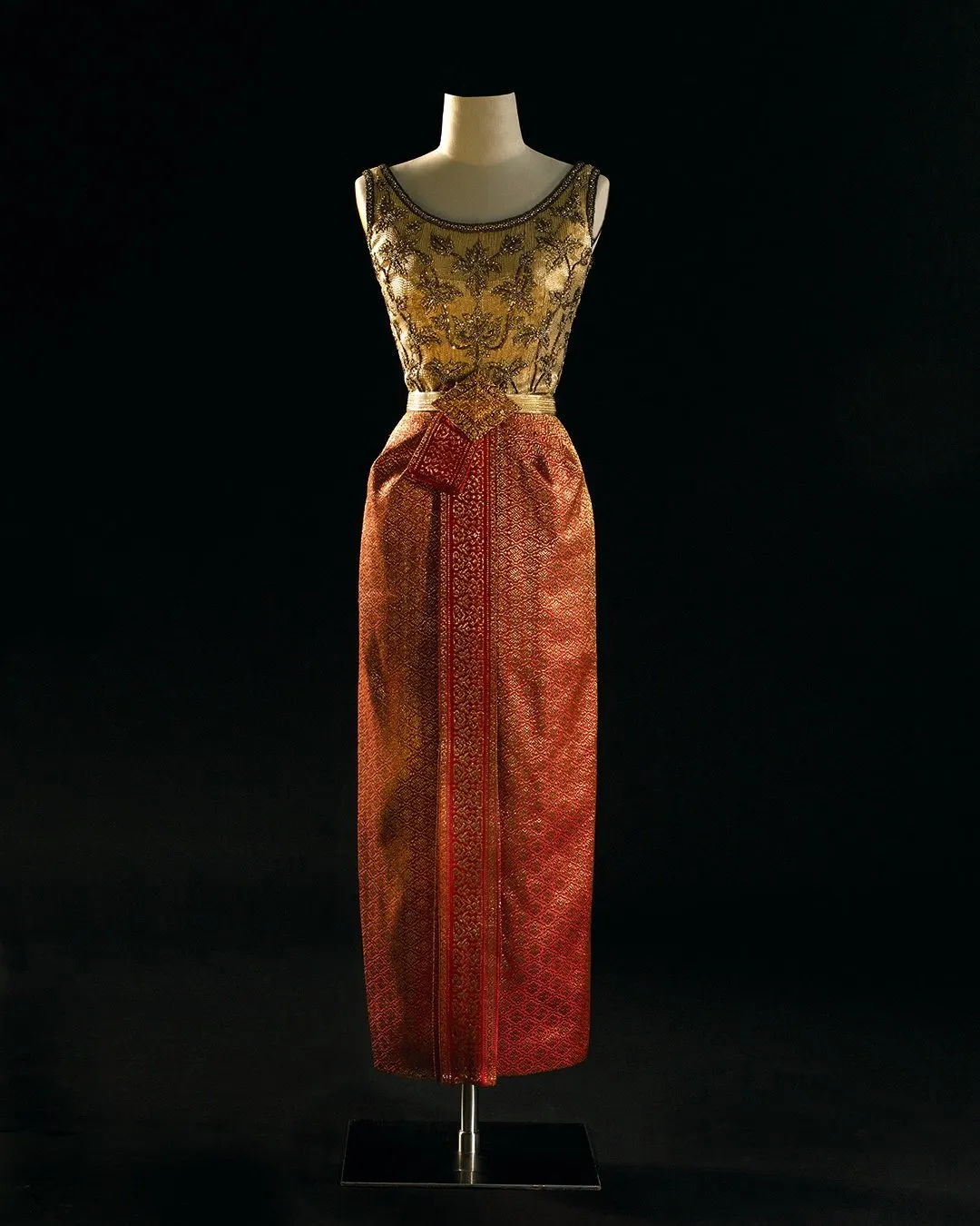A gold version of the Dusit Thai dress with sleeveless blouse and collar widens into a round neck and backline, on display at the Queen Sirikit Museum of Textiles.