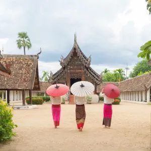 A group of women wearing Thai traditional dresses and holding paper umbrellas in front of a temple in Chiang Mai, Thailand