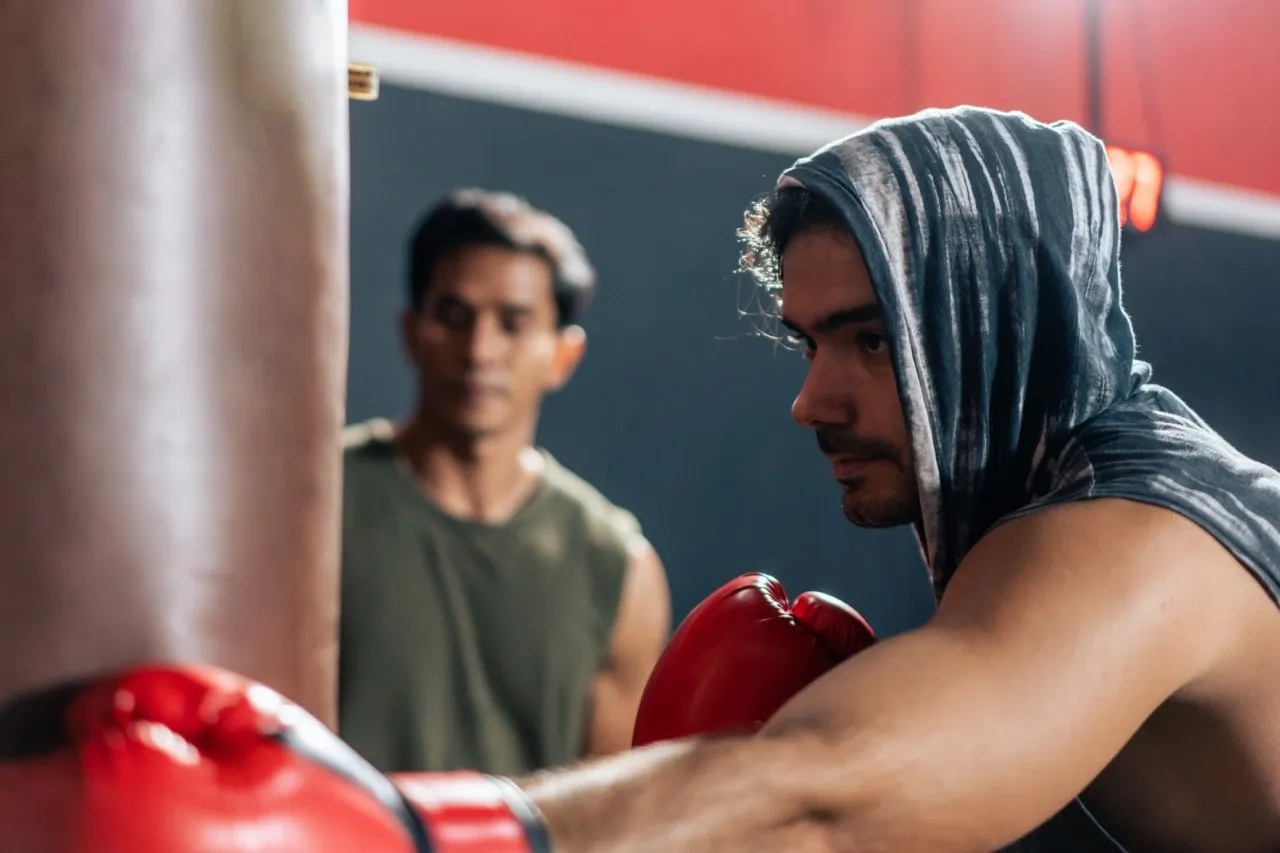 A man practicing boxing with a boxing trainer in the gym