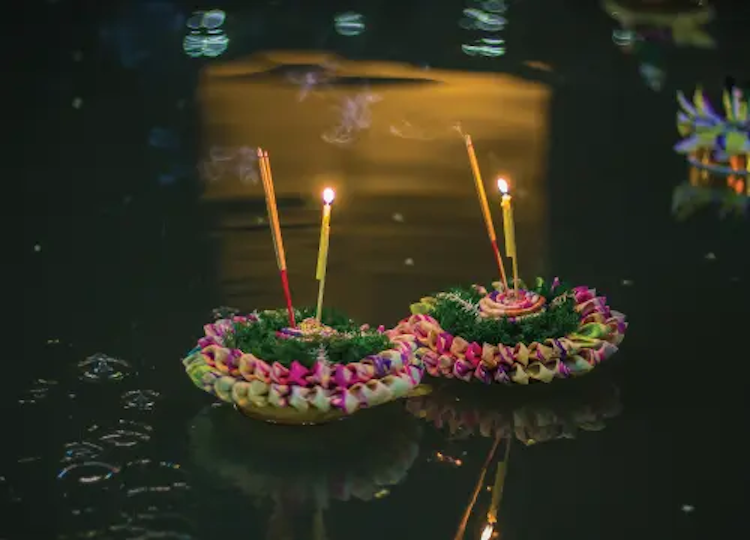 two candlelit krathong baskets floating in a river