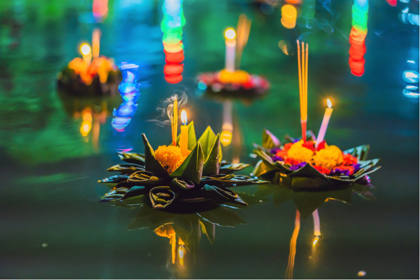 several candlelit krathong baskets floating in a body of water at night