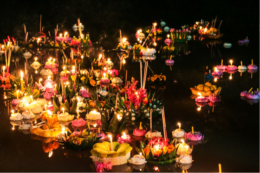 several candlelit krathong floating in a body of water, clustered together