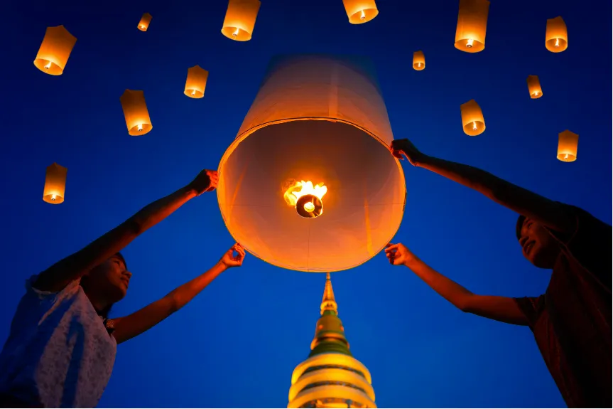 a man and woman holding a sky lantern just before releasing it into the night sky, with a Buddhist stupa peaking from the bottom of the image
