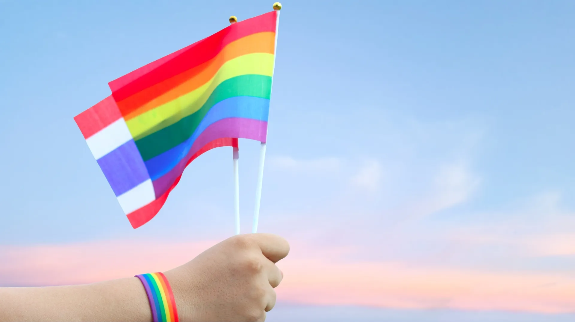 A hand holding the LGBTQ flag and Thai flag