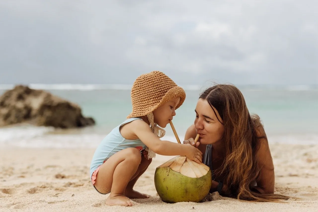 A shot of mother and daughter drinking coconut water on a beach