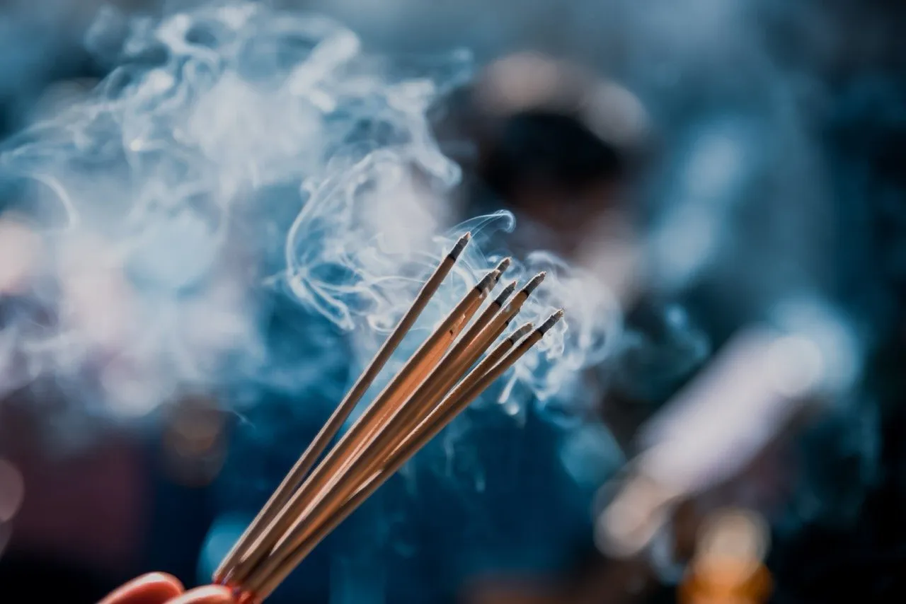 A close up shot of hands holding incense sticks to worship