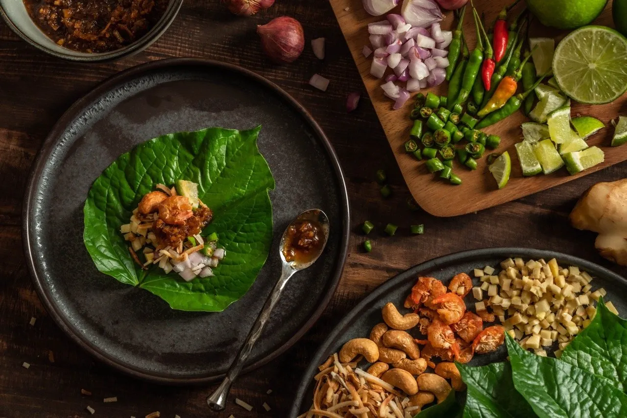 Thai herbal appetizer or Miang Kham consisting of dried shrimp, roasted coconut, ginger, lime, chili, and many herbs into fresh wild pepper leaf
