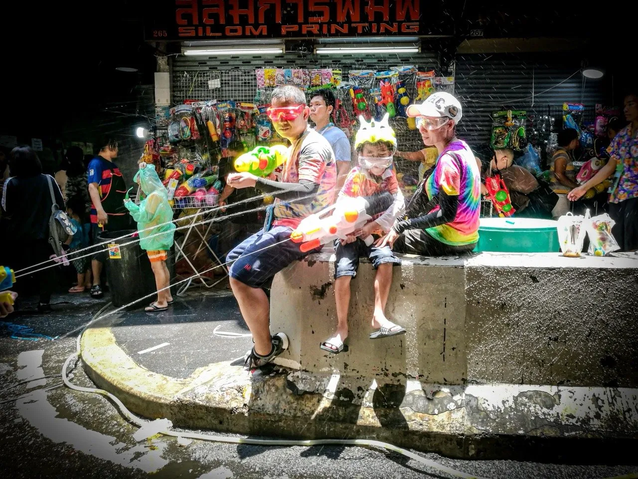 A family enjoying Songkran festival with water guns, goggles, and helmets