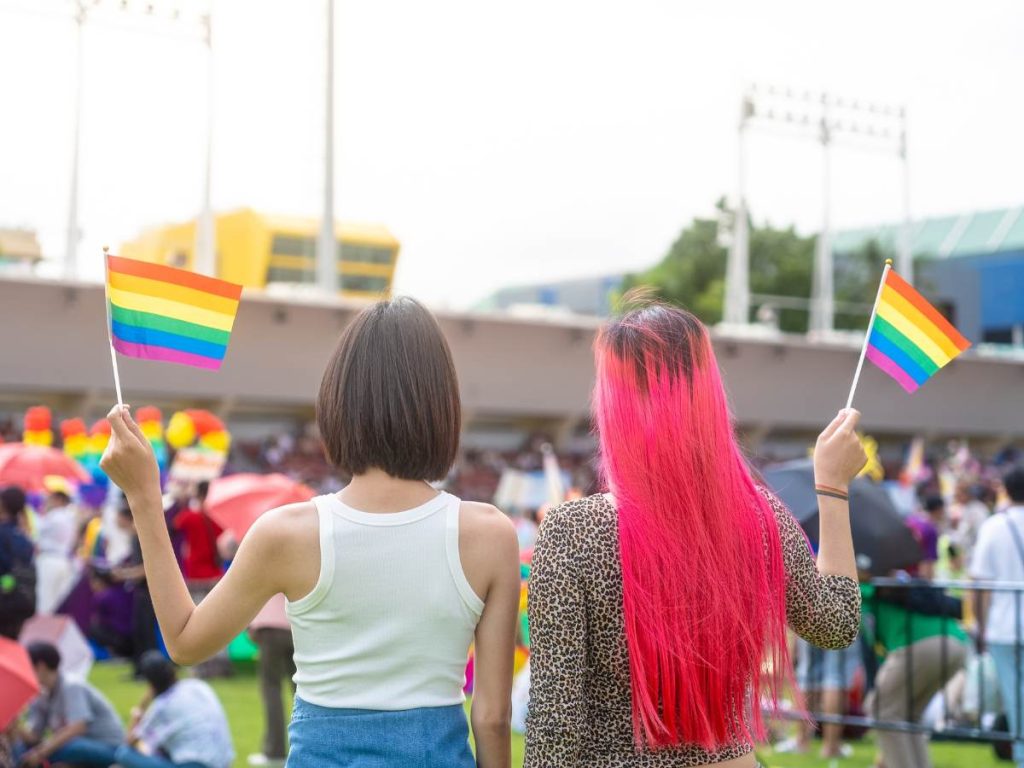 Two women waving rainbow flags at the Bangkok Pride Parade
