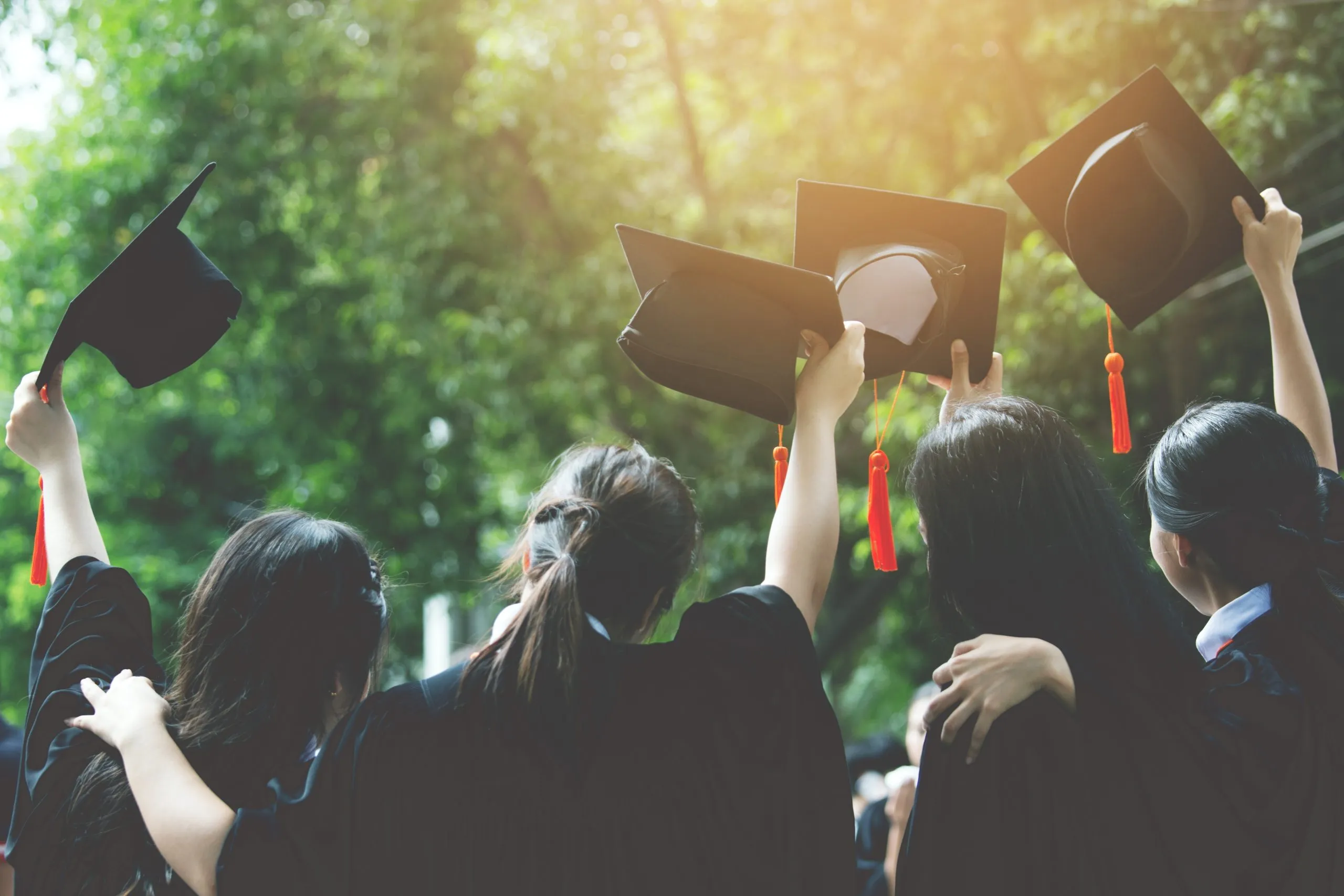 Four students raising their graduation caps.
