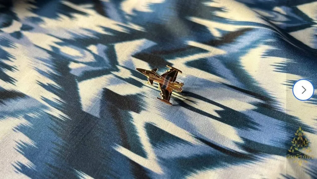 A metal pin of a Gripen fighter jet atop the original Mudmee silk pattern, "Mae Yanang Gripen."
