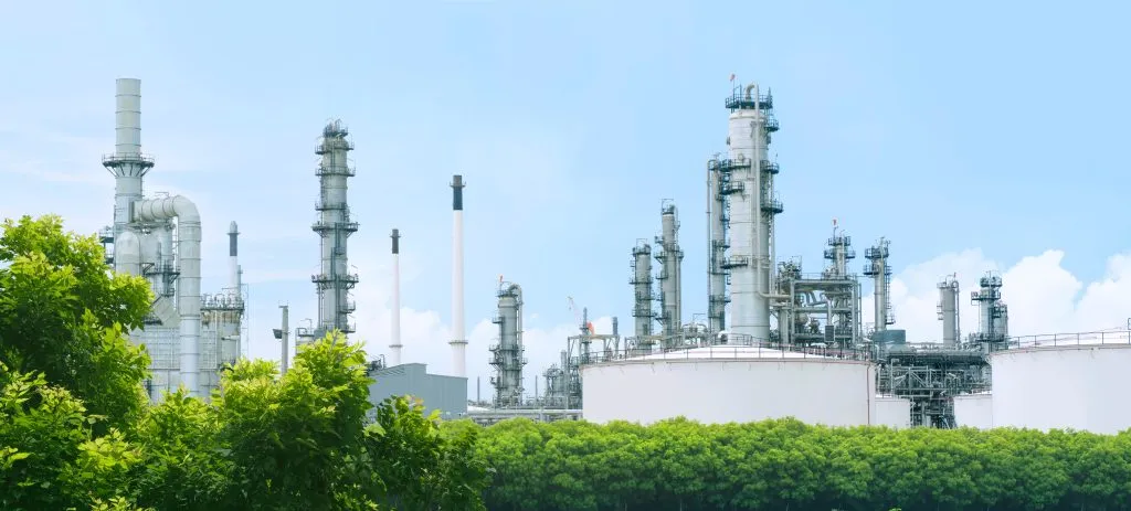 Oil refinery plant from industry zone with lush green trees and blue sky.