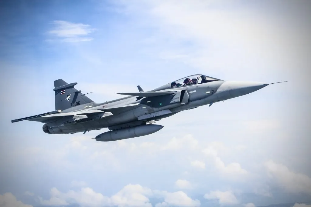 Saab Gripen fighter jet in flight over clear blue skies and pillowy white clouds.