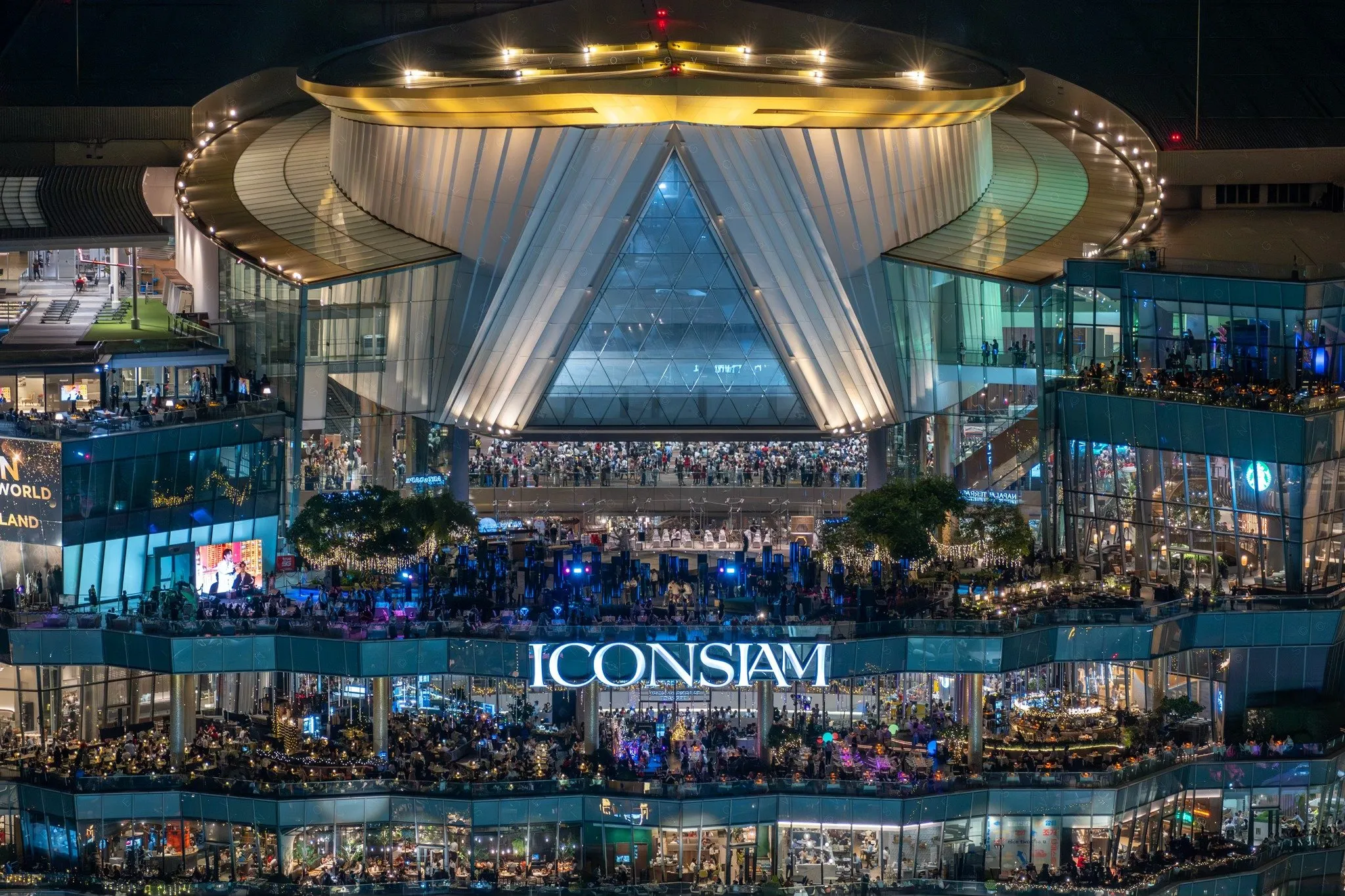 a distance view of ICOSIAM building with massive of crowd filling the building in the evening.