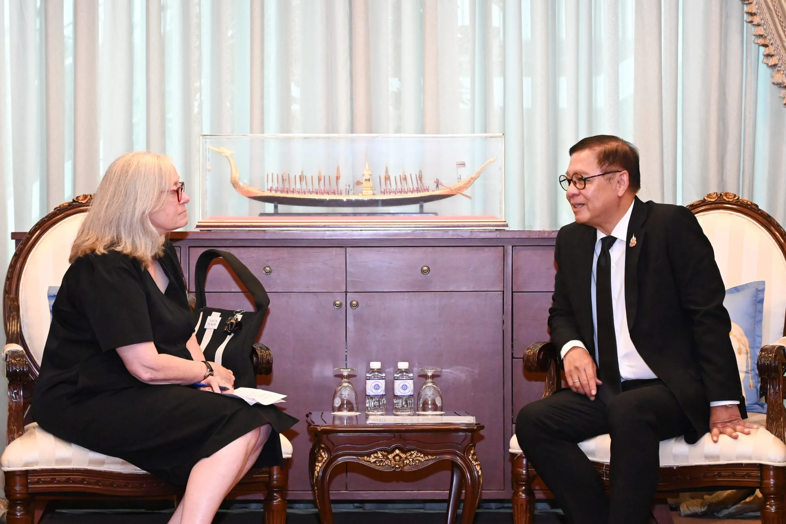 female caucasian diplomat sitting in a guest room talking to a male senior asian diplomat in a suit.