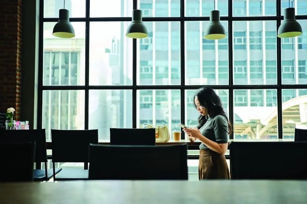 a lone female walking while looking at her phone. she appeared to be in a coworking space.