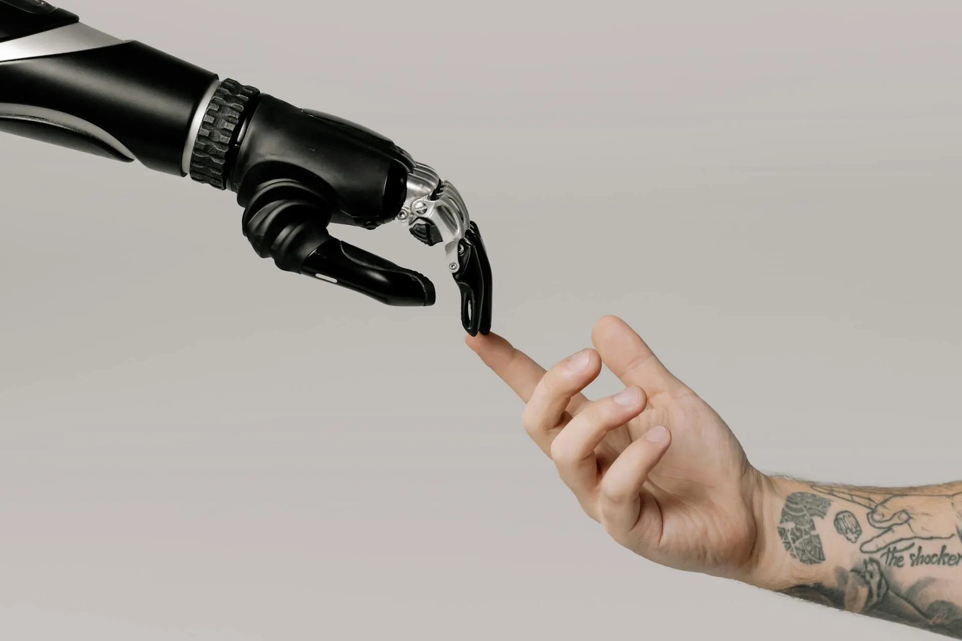 black robot hand extend from the left side of the screen, its index finger touches a human's index finger extended from the right side of the screen. the human arm has a tattoo.