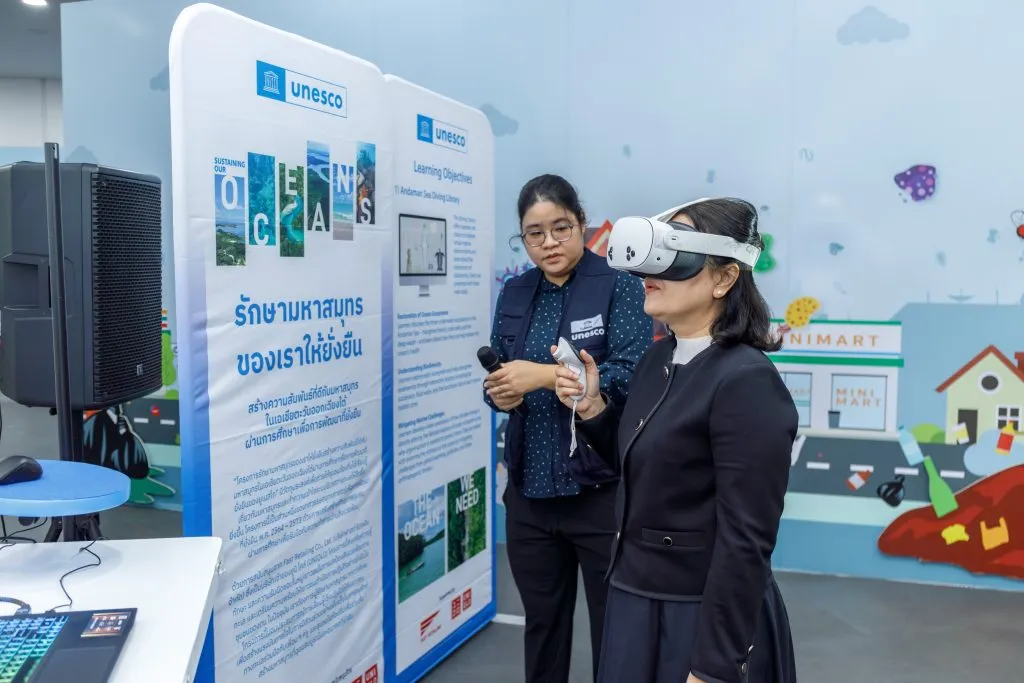 a woman wearing a vr head set standing next to another woman. they are appeared to be in the an exhibition.