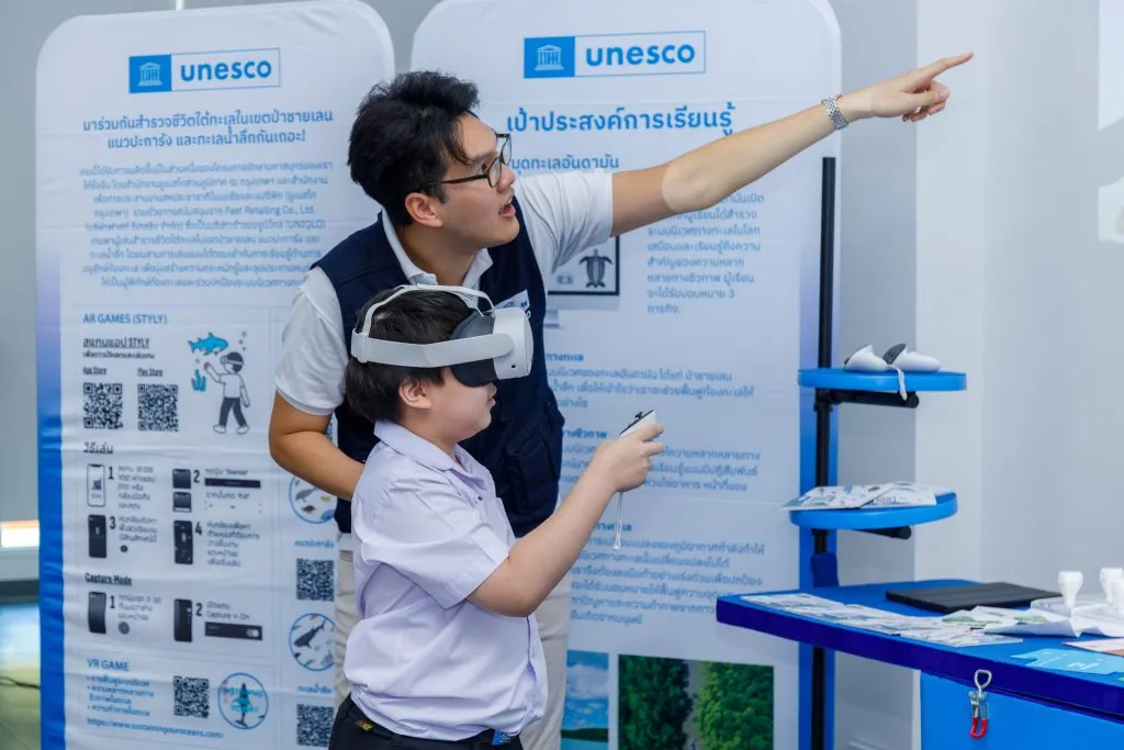 a unesco staff giving instruction to a young boy who is wearing a vr headset.