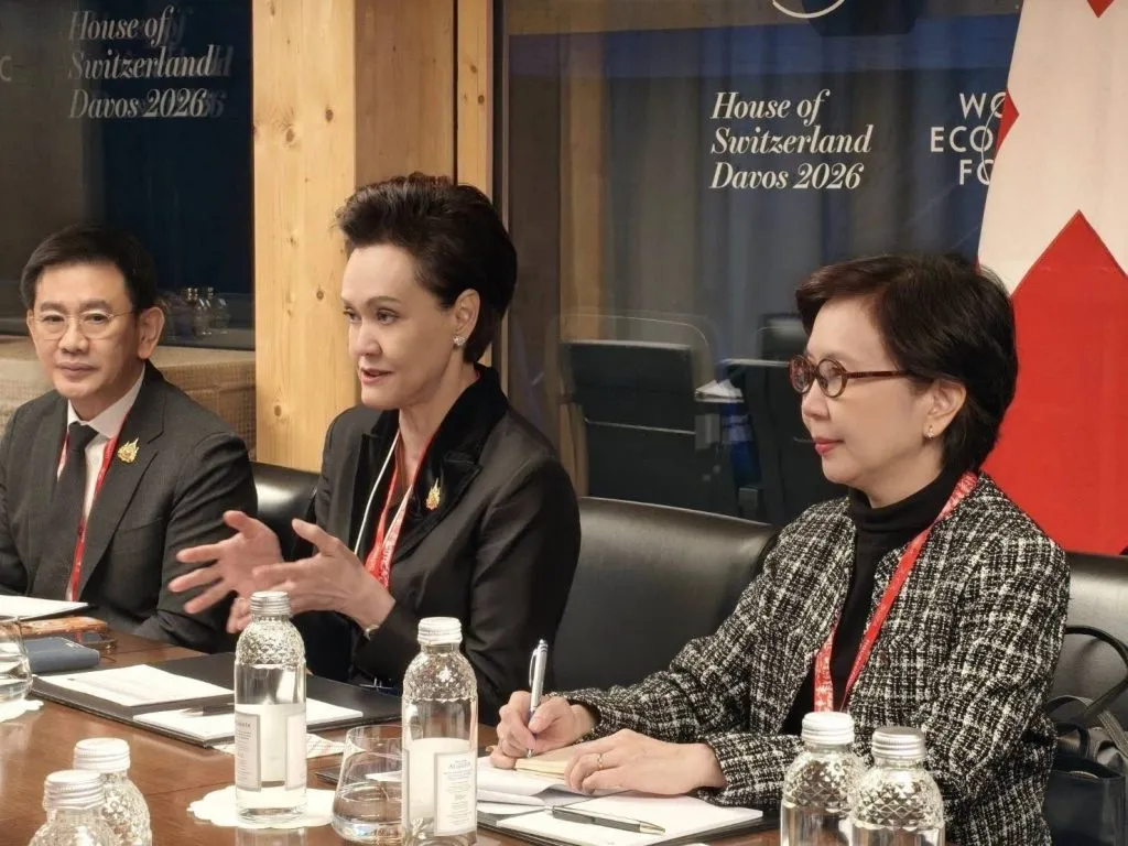 Three Thai professionals sit at a table in Davos 2026. A central woman gestures while speaking, flanked by a man and a note-taking woman.