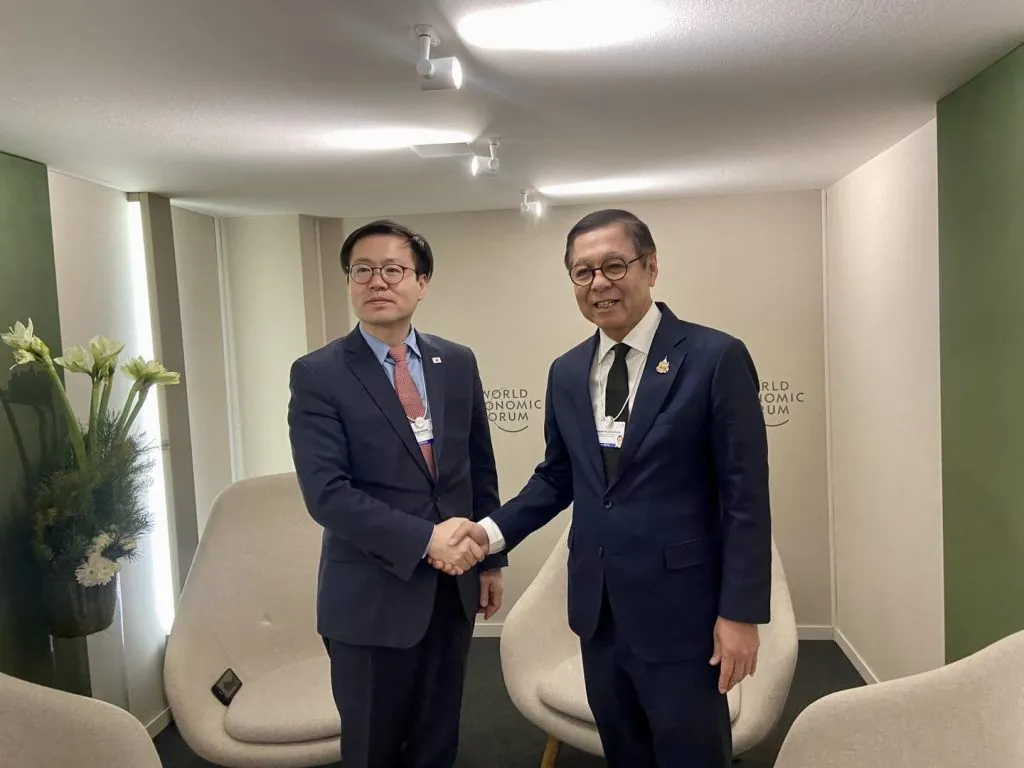 Officials shake hands in a bright room branded with World Economic Forum logos and decorated with elegant white lilies.
